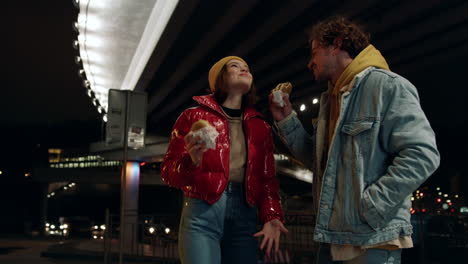 Pareja-Positiva-Comiendo-Bocadillos-Por-La-Noche.-Hombre-Alimentando-A-Una-Mujer-Debajo-Del-Puente.