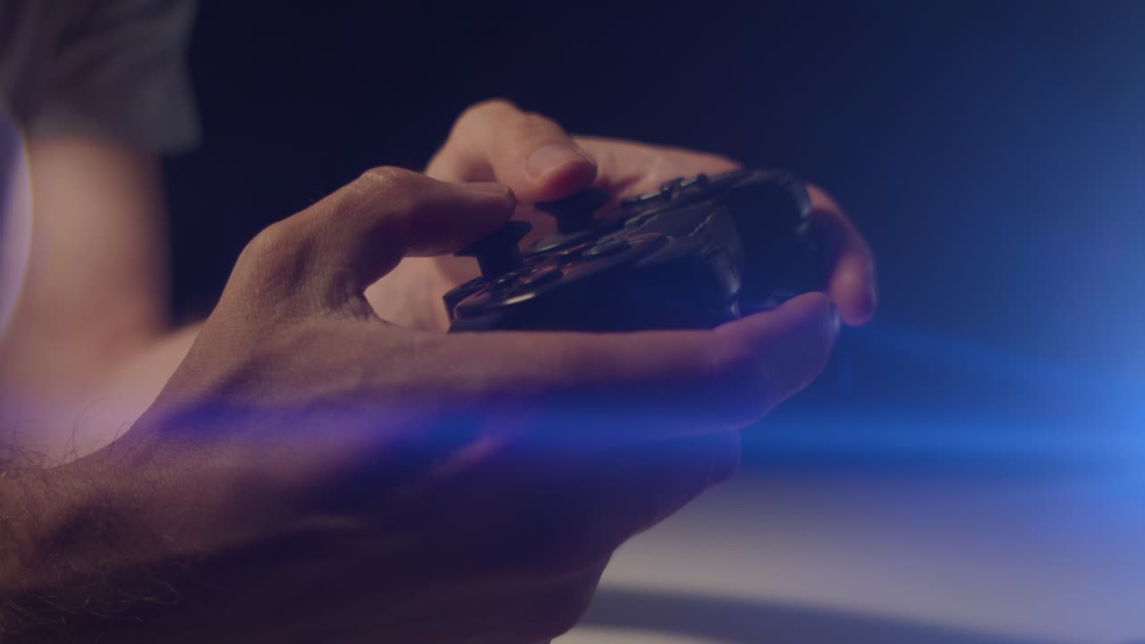 Playing video games in a darkened room with an anamorphic lens flare on a small controller playing slowly close up