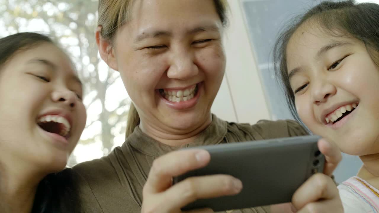 4k 아시아 여성이 딸들과 함께 스마트폰에서 게임을 하고 행복한 시간을 보내고 있습니다.