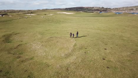 aerial-view,-three-people-on-stand-on-a-grassy-field-in-Connemara,-Ireland