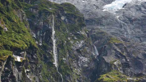 cascada extrema estrellándose contra las montañas rocosas de nueva zelanda con nieve en el pico - glaciar rob roy, nueva zelanda