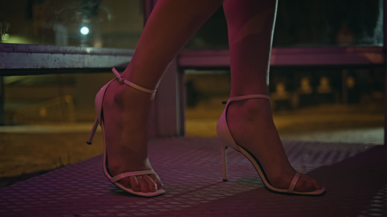 Party woman feet stepping neon town at evening closeup. Girl standing call box