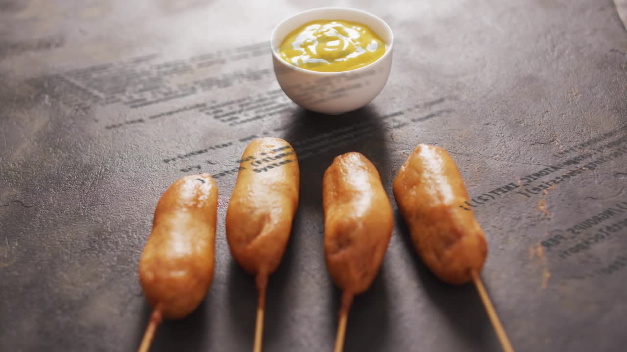 Camera shifting focus from blur to crisp corn dogs and mustard bowl, emphasizing texture in 3D