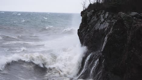 rough stormy waves crash against granite coastal cliff in slow motion