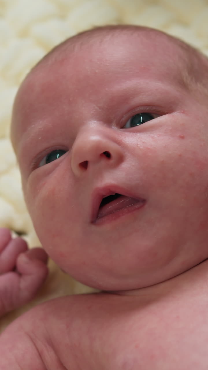 Primer plano del rostro de un bebé recién nacido con ojos azules y piel suave descansando sobre una manta con textura