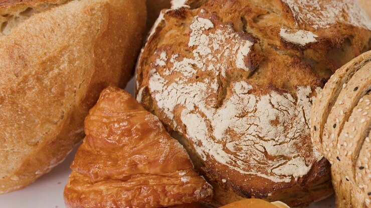Slow zoom out reveals various crusty sourdough loaves, croissants, and baguettes under bright studio lighting.
