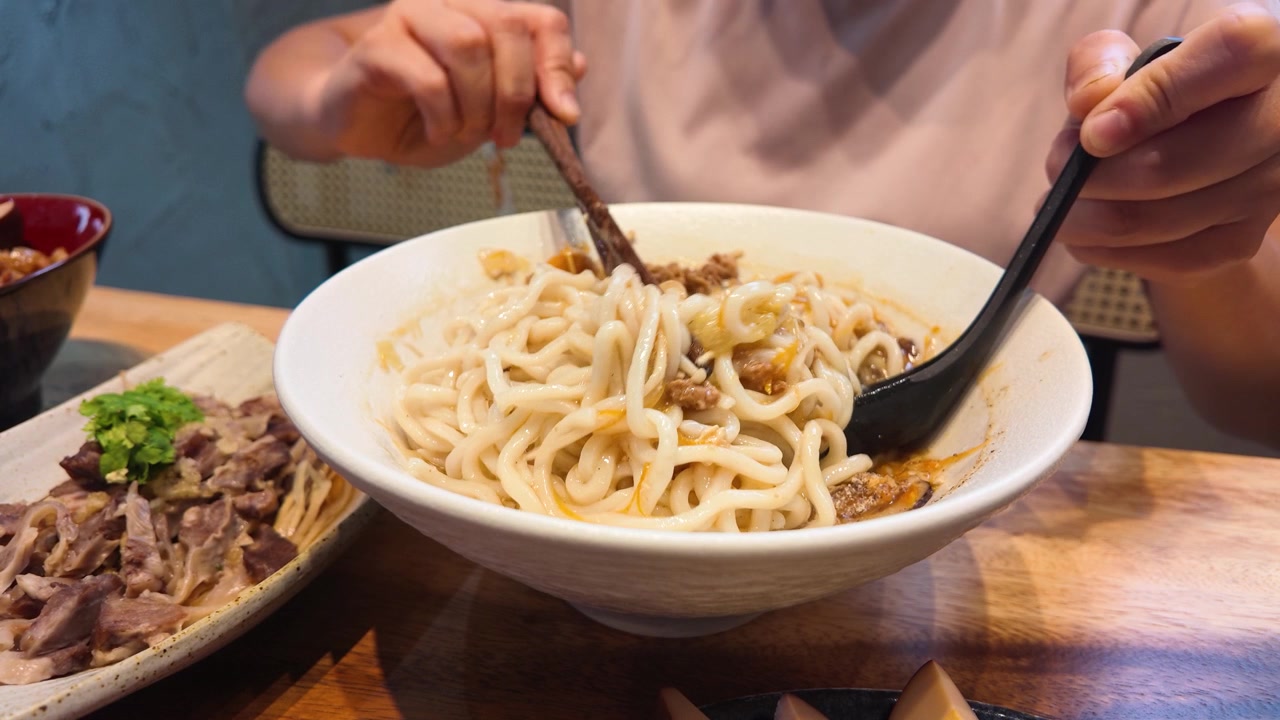 Primo piano di mani che usano bacchette e un cucchiaio per mescolare noodles piccanti a Bangkok