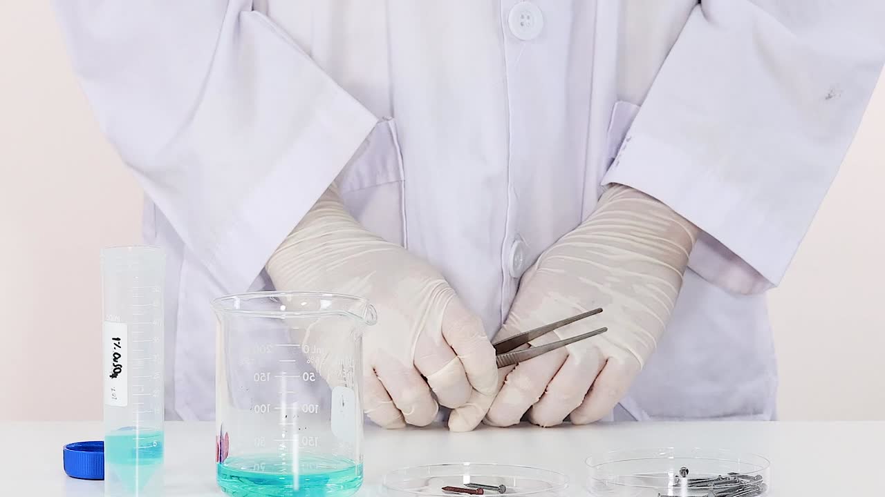 A scientist uses tweezers to manipulate metal pieces in a laboratory setting.