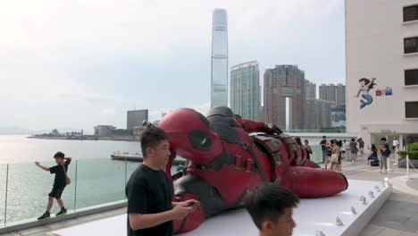 the 8-meter deadpool installation in hong kong, promoting disney’s "deadpool and wolverine" film, attracts tourists and locals with the city's skyline visible in the background.