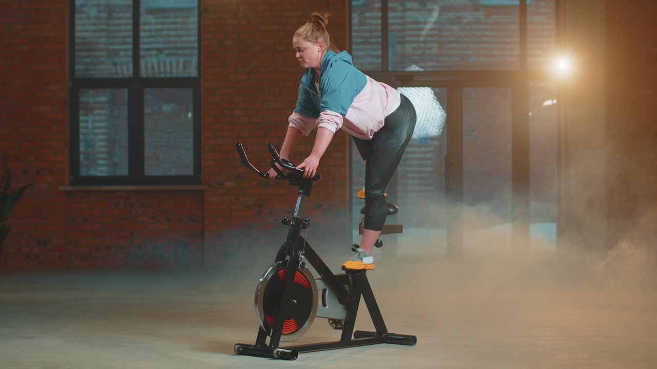 안개 가득한 체육관 에서 자전거 를 타고 에어로빅 라이딩 훈련 을 하는 운동 여자