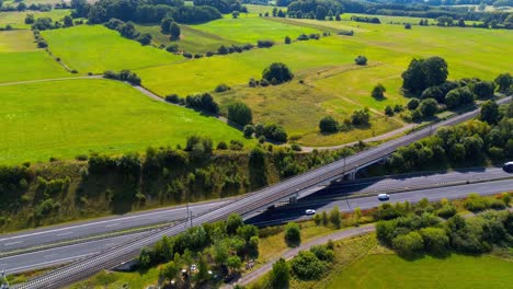 Aerial Drone View of Railway Bridge Crossing Highway Surrounded by Green Countryside Fields