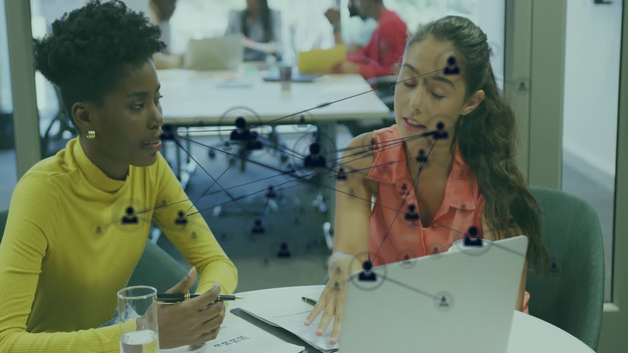 Woman in coral pointing at laptop, initiating tech icons showing links on glass, peer taking notes