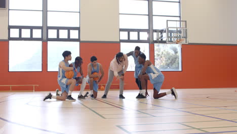 multiracial male basketball players with coach huddling and giving instructions to players in gym