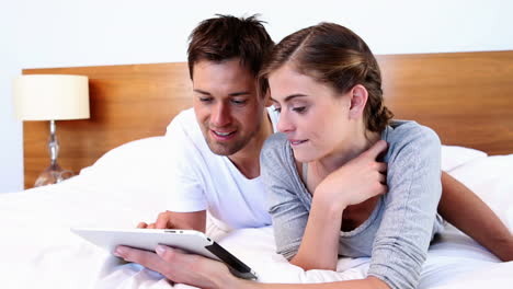 Happy-couple-lying-on-bed-using-tablet-together