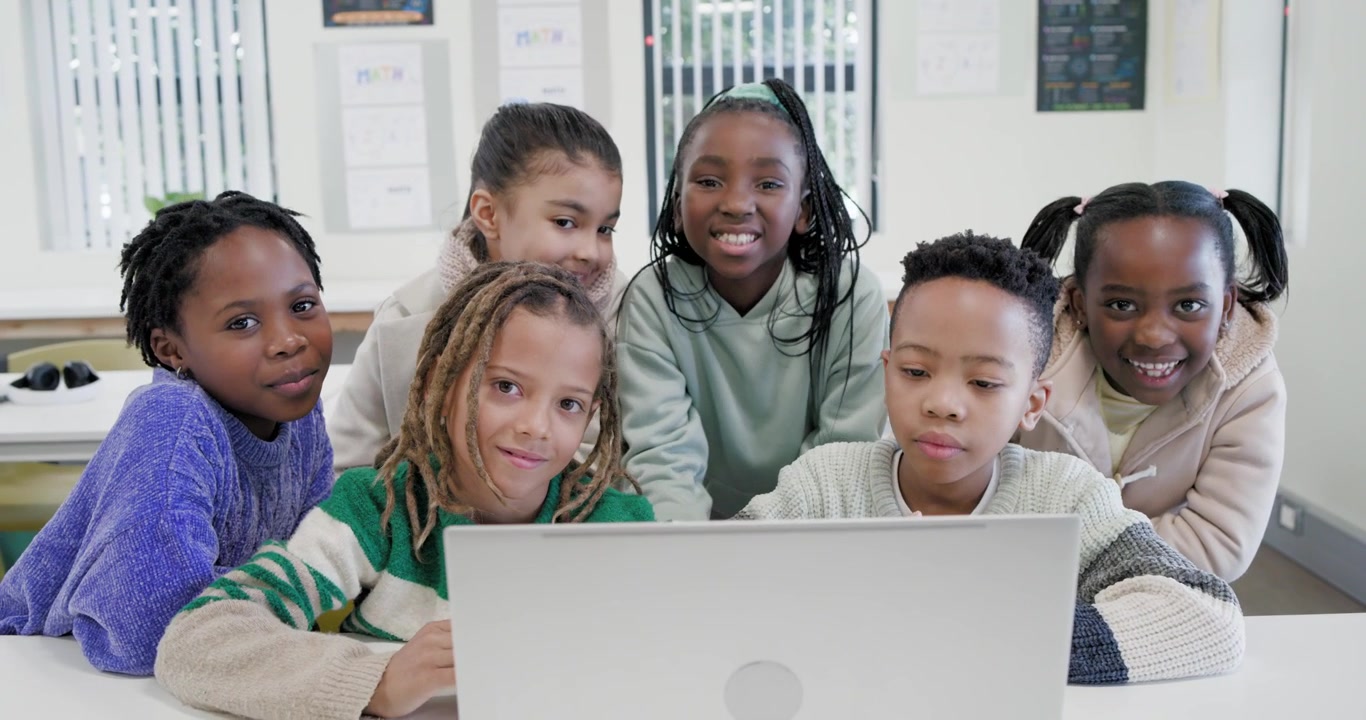 Bambini di varie etnie chinati su un laptop in classe, con il bambino in primo piano che lo utilizza, lavorando a un progetto.