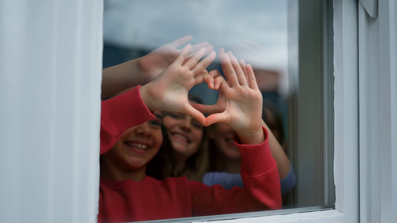 Niños felices formando un corazón con las manos a través de la ventana