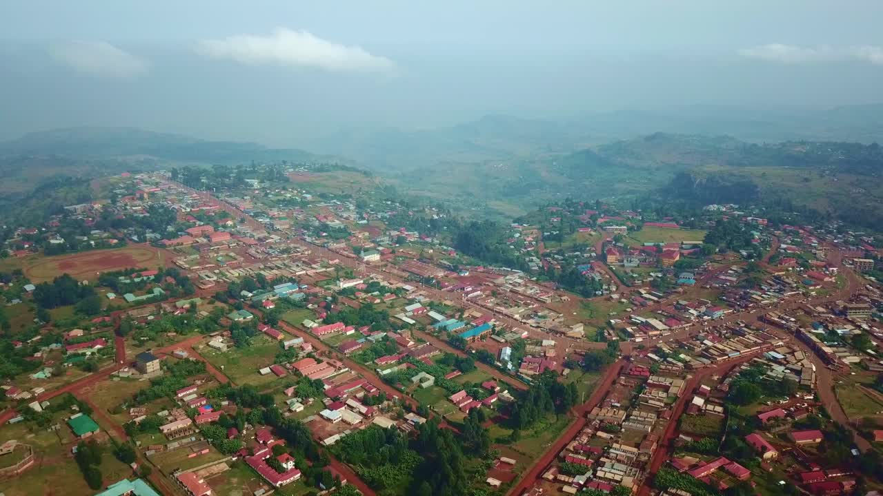 Drone image of Kapchorwa town featuring red soil roads, scattered buildings and mountain ridges in the distance, nestled on the green slopes of Mount Elgon in Eastern Uganda during wet season