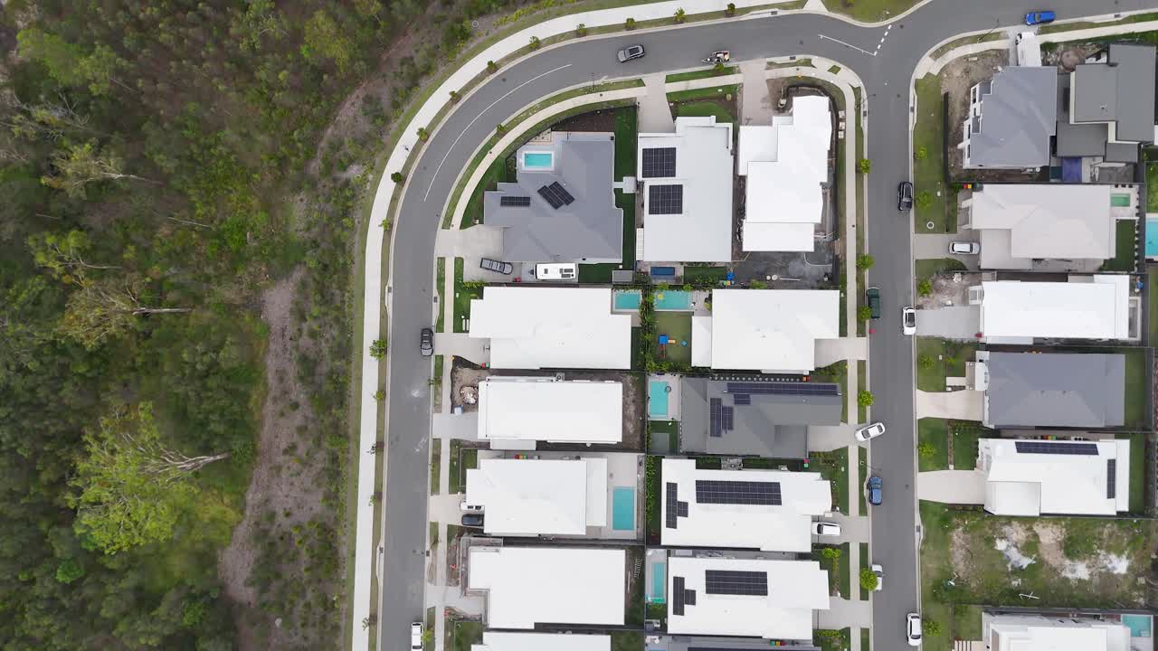 La videocamera di un drone sorvola moderne abitazioni suburbane accanto a una lussureggiante foresta, cielo nuvoloso, movimento fluido