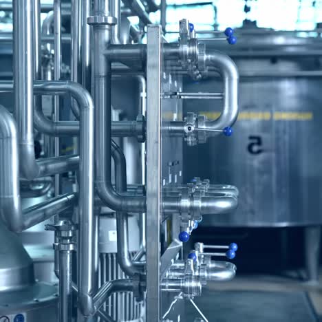 Silver tanks and cisterns at industrial production line in modern milk factory. Steel pipes and valves close up