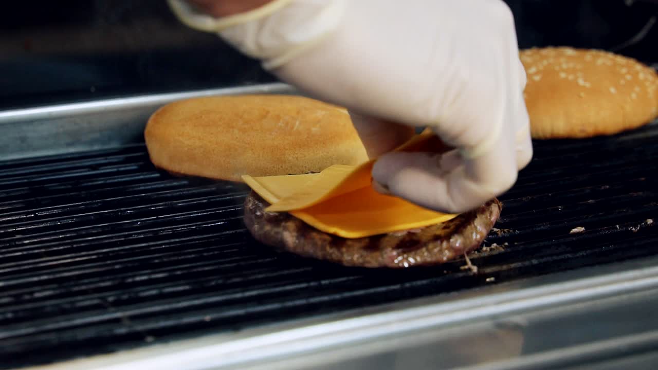 Cheeseburger preparation. Burger components frying on hot grill. Professional cook puts slices of cheese on a cooking cutlet. Cooking street food. Close-up