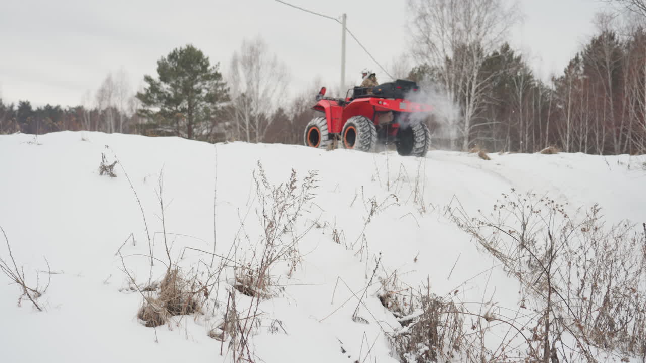 ATV rosso che salta su un argine innevato. Pilota bianco con giacca mimetica e casco accelera attraverso un campo di neve fresca vicino a una pineta, spruzzi di neve e azione acrobatica dinamica, adrenalina da ATV estremo