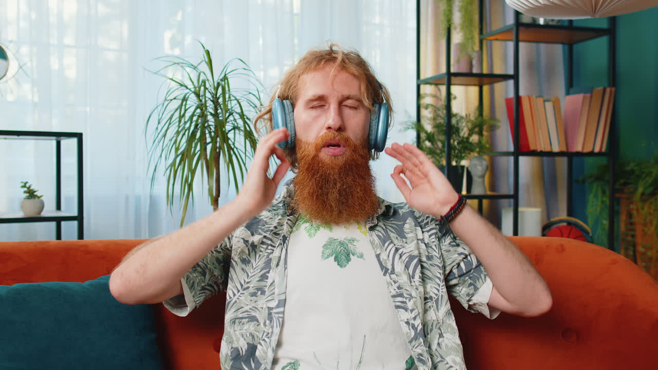 Redhead man listening music breathes deeply meditating with concentrated thoughts peaceful at home