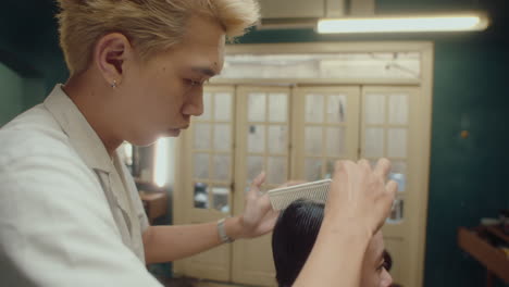 asian barber parting hair of man with comb
