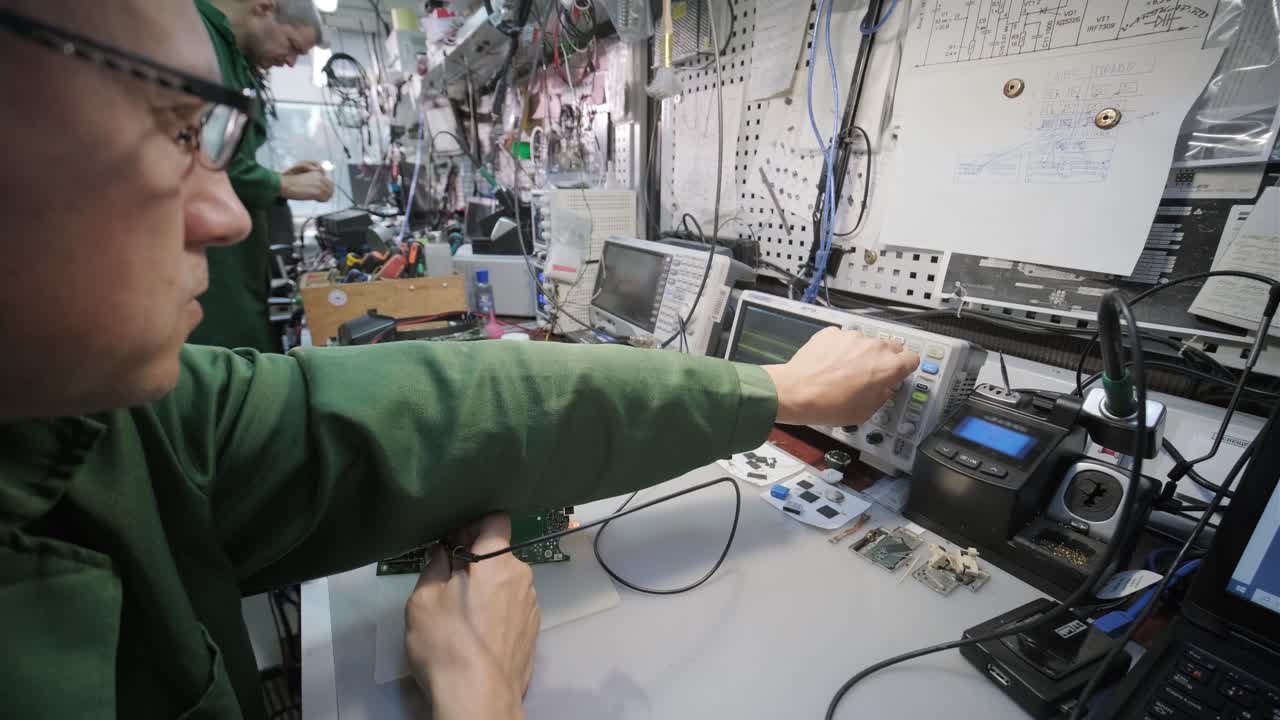 tienda de reparación de equipos electrónicos. el técnico ingeniero soldada la placa de circuitos impresos de un dispositivo electrónico bajo un microscopio.