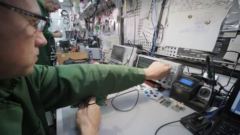 electronic equipment repair shop. the engineer technician solders the printed circuit board of an electronic device under a microscope.