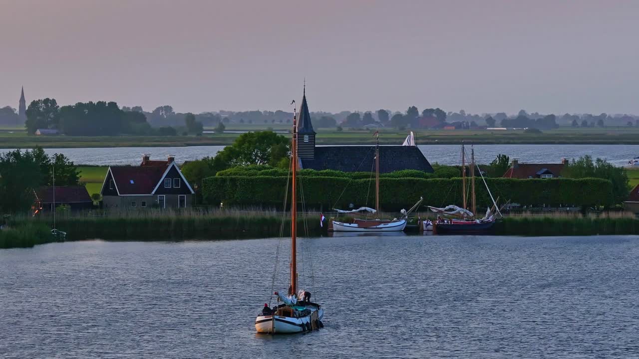 Vista aerea di un bellissimo tramonto dorato sul lago con chiesa e barca a vela a Sandfirden, Frisia.