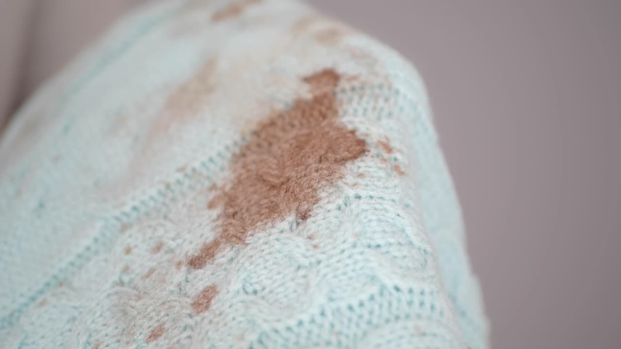 Prst ukazující na hnědou skvrnu na světle modrém pleteném svetru.