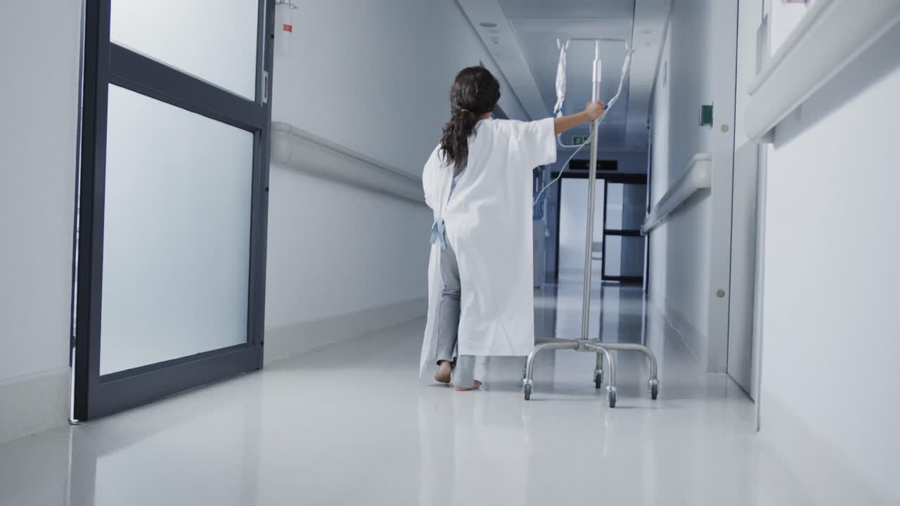 разовая больная девушка-пациент ходит с капелькой в больничном коридоре в замедленном движении
