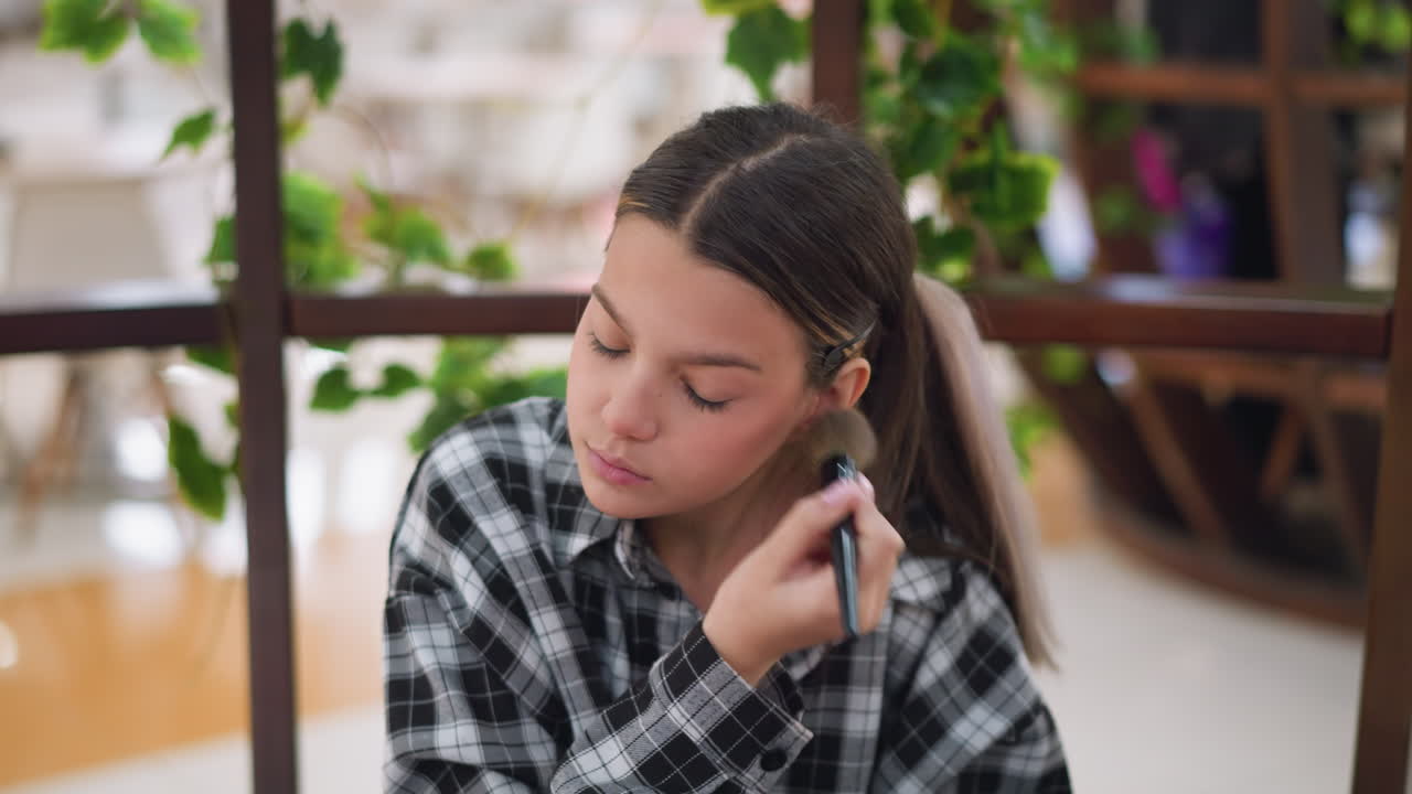 vista de cerca de una joven aplicando maquillaje en su mejilla izquierda usando un pincel, se centra en mejorar su belleza con trazos suaves, con un fondo natural y iluminación vibrante