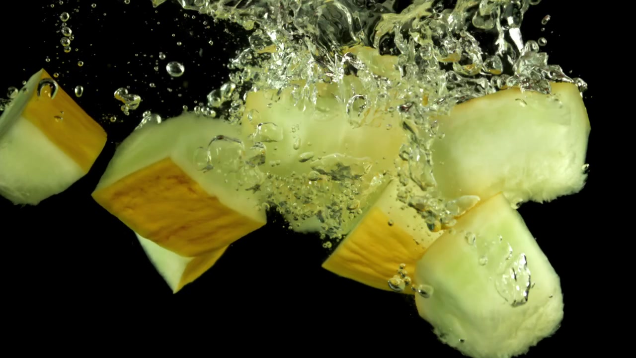 Friske melonbiter som plasker ned i klart vann i sakte film