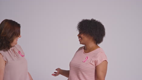 Studio-Portrait-Of-Two-Smiling-Women-Of-Different-Ages-Wearing-Pink-Clothing-And-Breast-Cancer-Awareness-Ribbons-Hugging-Against-White-Background-1