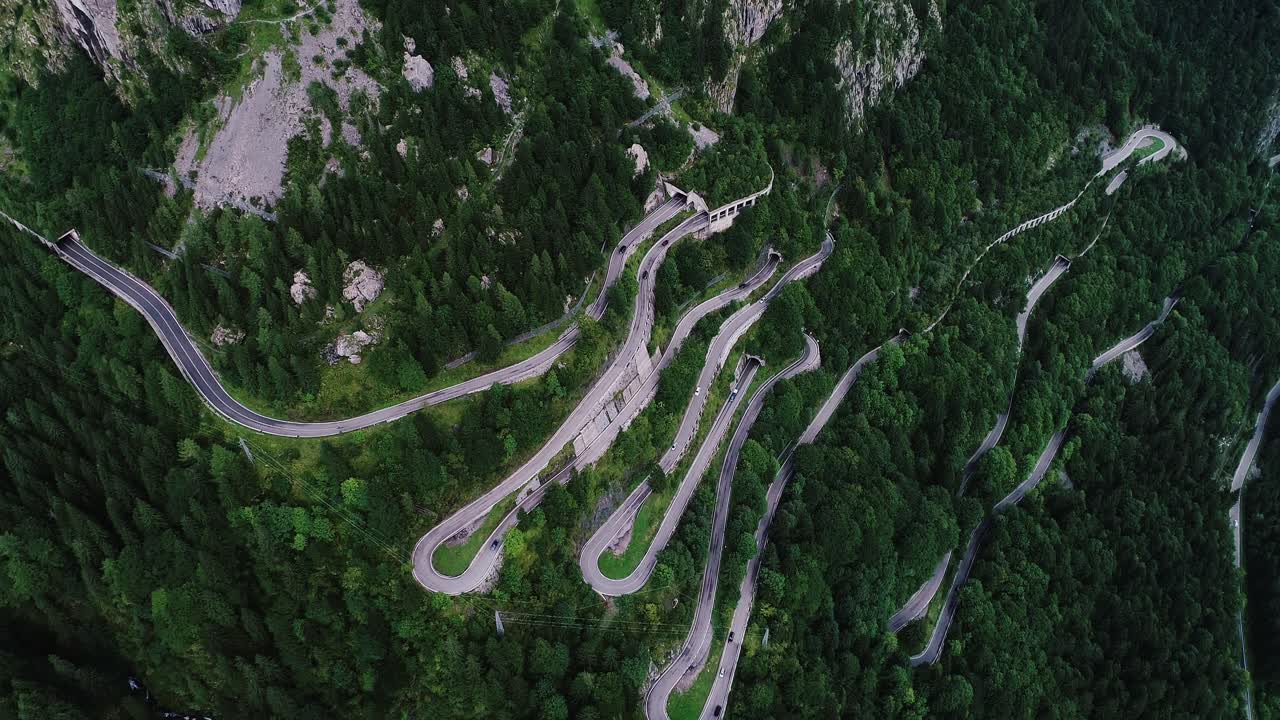 Drone reveals zigzag mountain road carving through steep alpine forest terrain