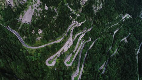 drone reveals zigzag mountain road carving through steep alpine forest terrain