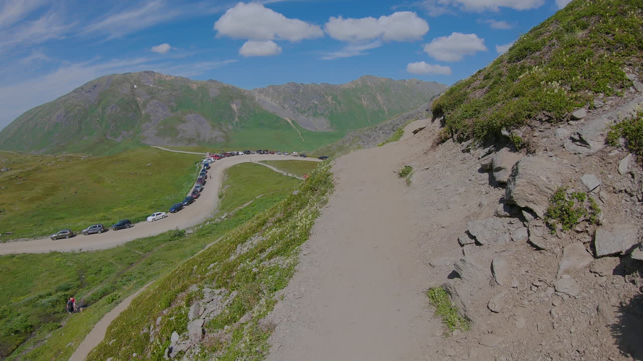 Walking Alaska's hiking trail overlooking cars parking along the road during a sunny day.