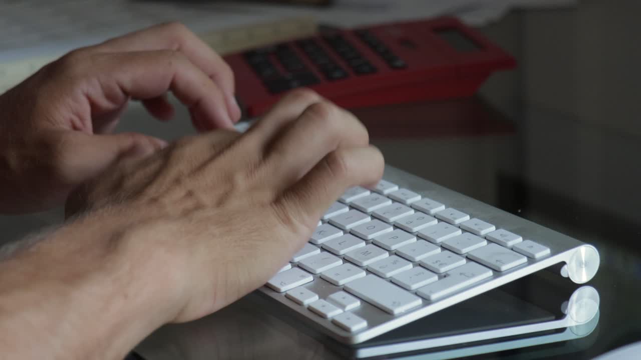 primer plano extremo de manos masculinas escribiendo en el teclado bluetooth en una mesa de vidrio con calculadora en segundo plano