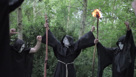 un culto se reúne en el bosque para realizar un canto ritual y el gran maestro levanta las manos con un bastón mágico