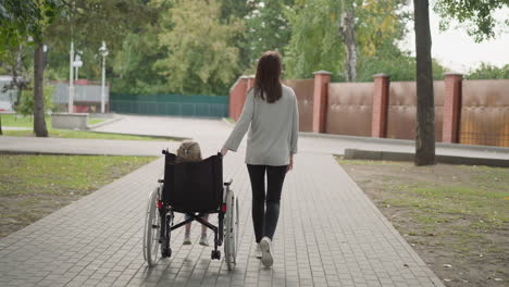 madre ayuda a la hija pequeña a moverse en silla de ruedas en el camino