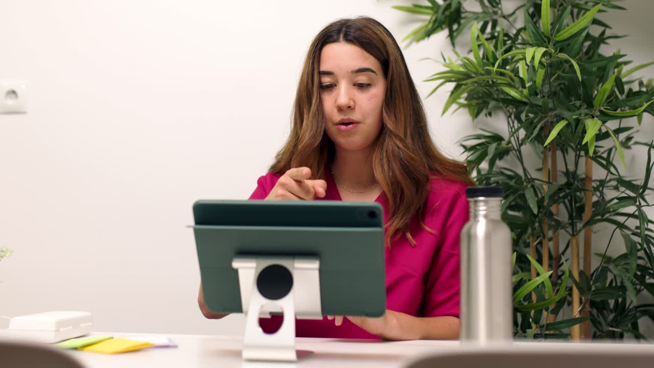 Mujer joven con uniforme médico hablando en videollamada con una tablet.