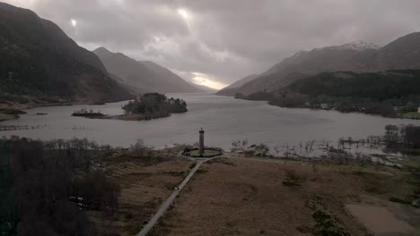 glenfinnan monument by the lake with scottish highlands in backdrop, overcast sky, aerial view