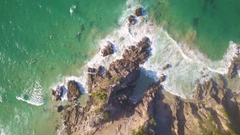 Drone-top-down-orbit-on-rocky-coast-and-cove-as-ocean-waves-break-on-Byron-Bay