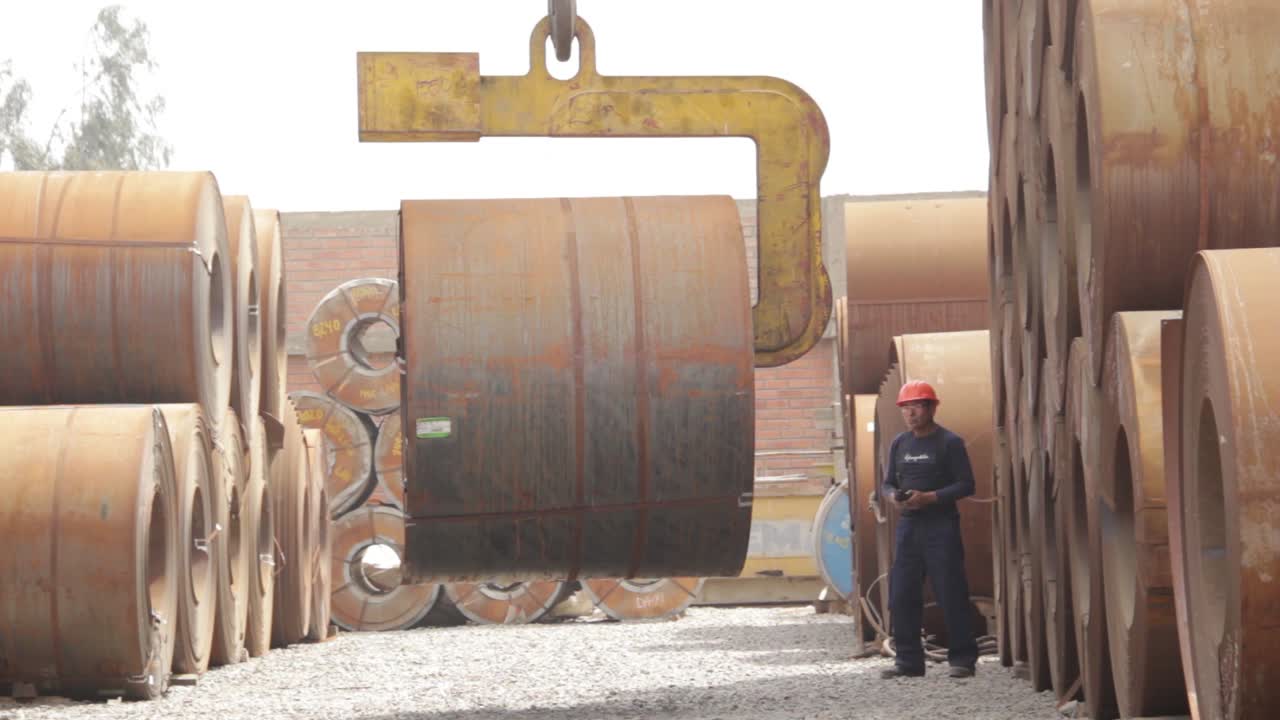 Overhead crane lifting heavy steel coils in the storage of a factory