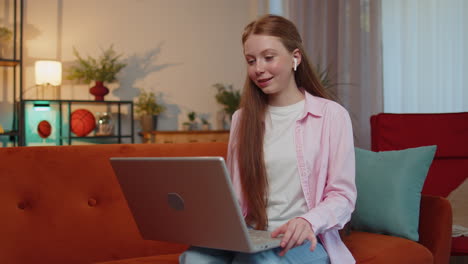 child girl sitting at home, looking at laptop, making video conference call with friends or family