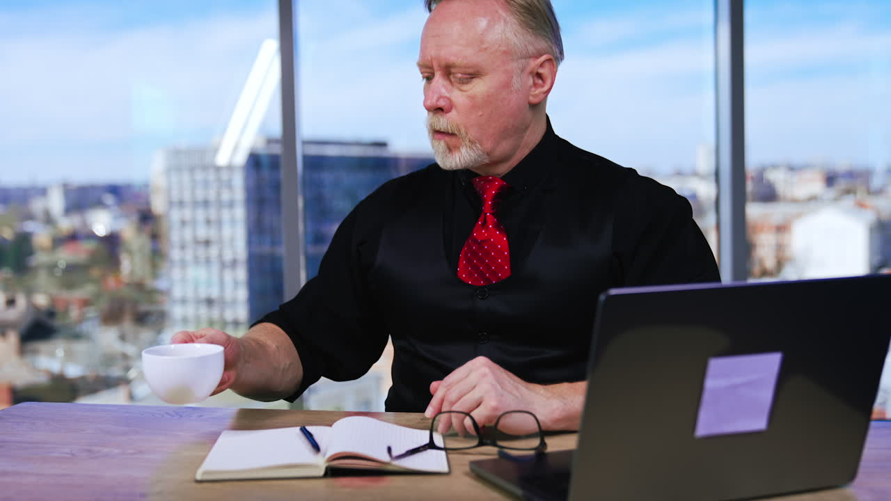 Annoyed man puts off glasses with irritation. Businessman feels tired from work, distracts from his laptop and drinks some coffee.