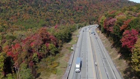 cars, trucks, traffic drive on highway turnpike through colorful autumn leaves