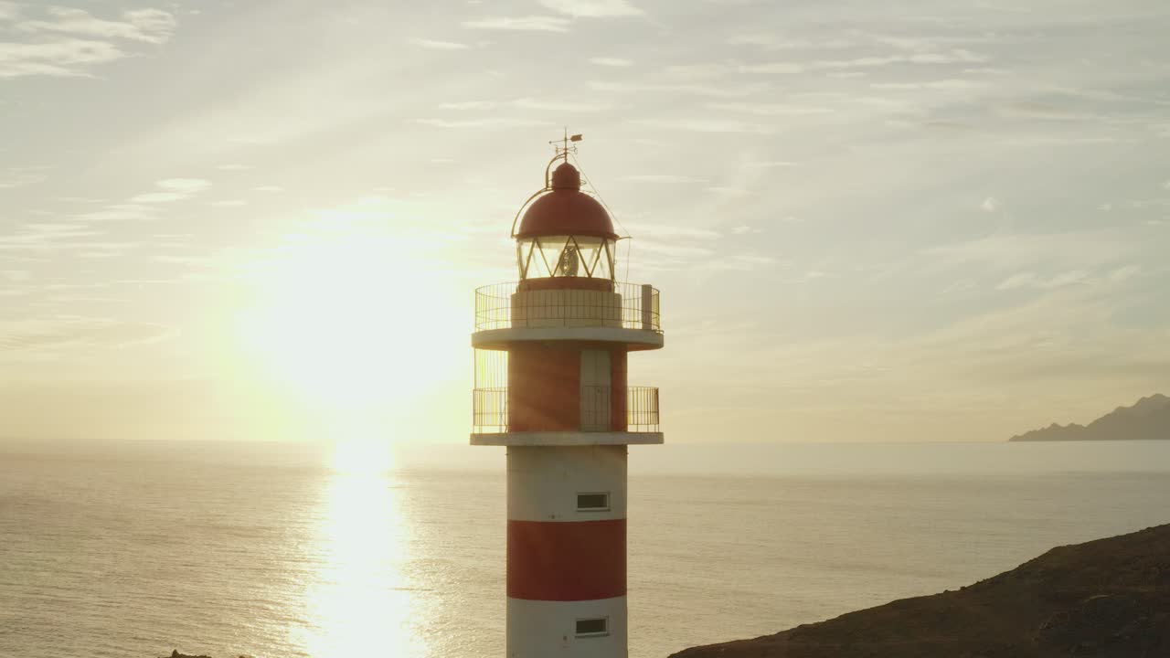 toma cercana de un faro con sol y océano en el fondo a la hora dorada