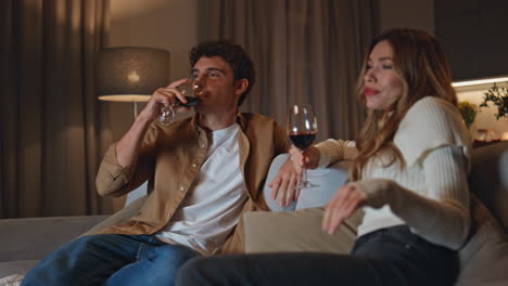Relaxed pair drinking wine on cozy home couch. Carefree young couple talking